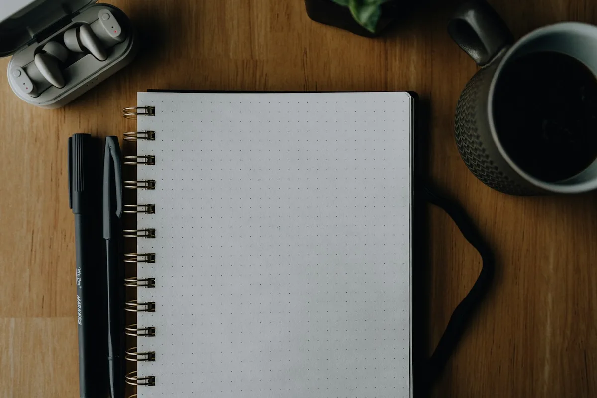 A blank notebook, pen and headphones on a wooden desk